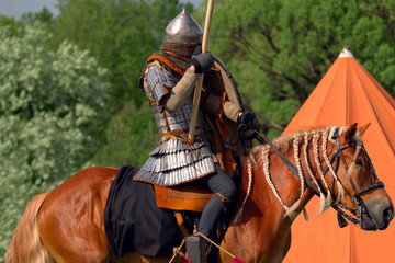 Knight in armor on a brown horse. A hero in chain mail with a spear stands guard. Warhorse with a...