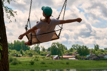 A happy girl of 10-12 years old swings on a chain swing in the summer in the village. The swing...