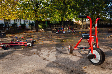 des tricycles dans la cour d'une école. Des tricycles rouges dans une aire de jeu. Des vélos pour enfant. Une cour d'école sans enfant. Une cour de récréation vide. - obrazy, fototapety, plakaty