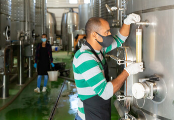 Man worker of winery in protective mask checking wine production process at fermentation tank