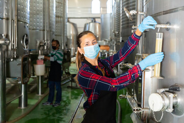 Female winemaker in protective mask analyze the white wine in a beaker
