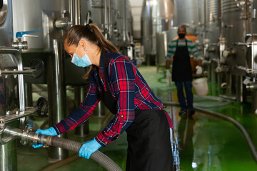 Female worker works at a winery, filtering wine in barrels