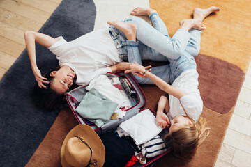 Mother and daughter dreaming of a travel, lying on the floor, packing a suitcase