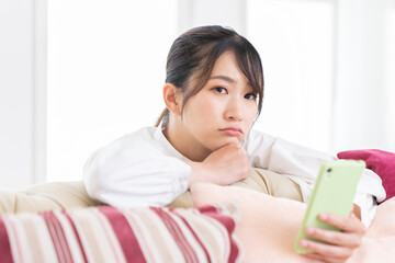 部屋でスマホを見る女性　考える