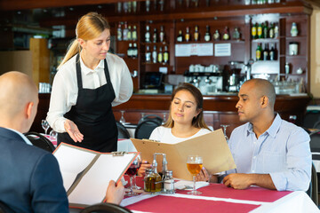 Polite young waitress taking order in pizza restaurant, helping guests in choosing meals from menu