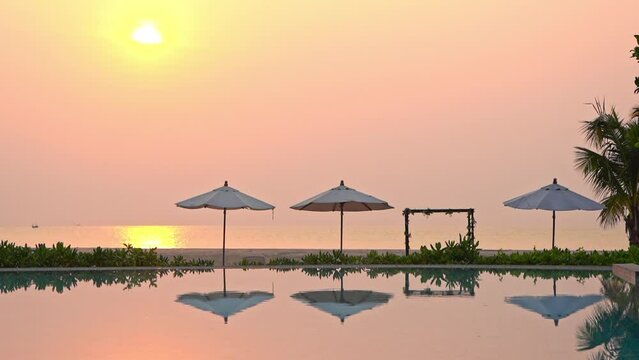 Swimming Pool in Tropical Resort, Parasols and Sky Mirror Reflection on Water at Sunny Evening