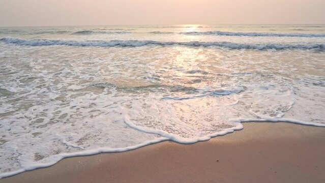 Crashing sea waves with foam rolling over wet sand at sunset beach with sunlight reflection on water in Bora Bora, French Polynesia
