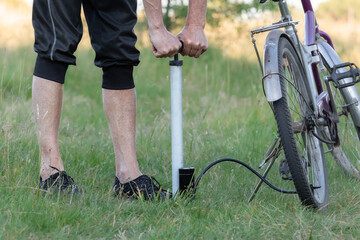 Obraz premium A cyclist pumps air into the wheel using a manual autonomous pump.Inflating the bicycle tire.The concept of bicycle repair.