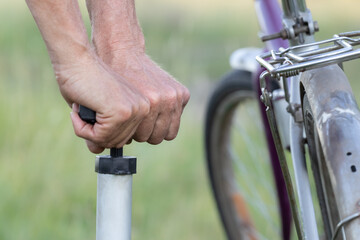 A man's hands inflate the tire of an old bicycle using an autonomous hand pump.Close up.