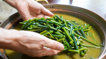 銅鍋と灰汁であく抜きをしている、鮮やかな緑色になった山採り天然わらびを持つシニア女性の手