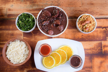 Feijoada typical Brazilian food, beans with pork bacon, orange rice and flour, chili sauce and...