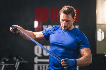 Portrait muscular sporty Caucasian man wraps his hands in blue sports bandages for training