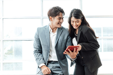 Obraz premium Business couple standing together checking work on tablet near the window background.