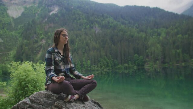 Wide shot of a Woman doing Yoga and Meditation on a rock surrounded by Nature in a Mountain Lake location
