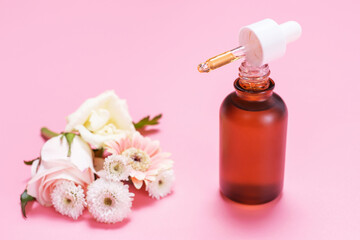 Obraz na płótnie Canvas Bottle and pipette with serum and flowers on pink background, natural cosmetics concept.