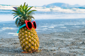 Funny pineapple in stylish sunglasses on a beach.