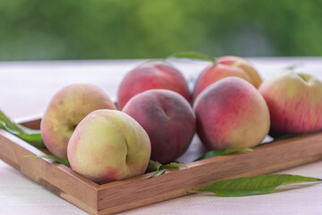 Fresh Sweet Peach on green bokeh background, Pink and yellow Peach fruit with leaf on wooden plate.