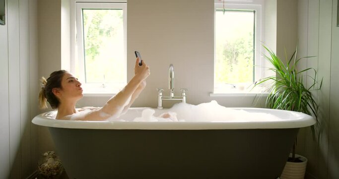 Young woman taking selfies with a cellphone during a bubble bath