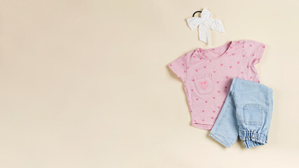 Children's pink T-shirt, folded jeans and elastic band for hair on a beige background. Copy space.