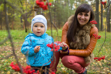 Cute Child Girl Walking in Autumn Park with Happy Young Mother, She is Surprised by Berries on the Rowan Tree