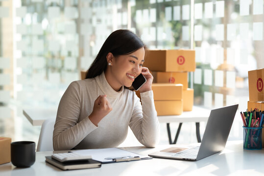 Online Sales Business Owner Woman Standing Talk On The Phone Looking At Laptop In Office. Happy Asian Business Woman Successful Excited Raised Hands Rejoicing.