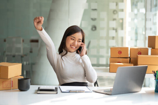 Online Sales Business Owner Woman Standing Talk On The Phone Looking At Laptop In Office. Happy Asian Business Woman Successful Excited Raised Hands Rejoicing.