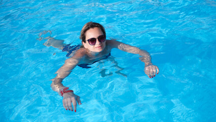 Woman in sunglasses swims in pool in summer