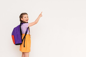A child with a satchel points with his index finger at your advertisement on a white isolated background. Preparatory summer courses for children. - obrazy, fototapety, plakaty