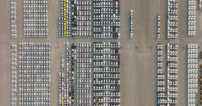 Aerial view of large parking new cars distribution center of modern seaport. Lot of vehicles waiting for sale and transportation shipping by freight cargo vessel ship. Automobile industry.