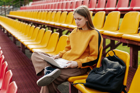 A young girl is doing her homework using a laptop in the stands of the stadium. The concept of training and education