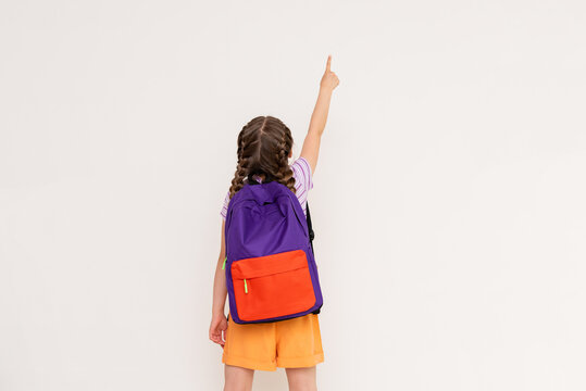 A child with a satchel points with his index finger at your advertisement on a white isolated background. Preparatory summer courses for children.
