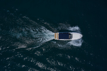 A white big boat with a blue awning is moving fast on dark water. Aerial view. Big white boat with an awning moving on the water top view.