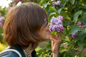 Fototapeta premium Close up portrait of beautiful woman smelling purple lilac