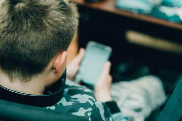 A boy 10s watches a video clip in a smartphone at home. Back view,closeup.Selective focus.