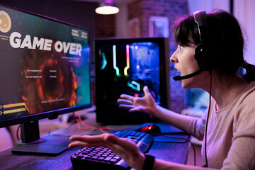 Young player losing video games tournament on computer, feeling sad about lost shooting gameplay competititon. Female gamer playing online rpg action championship on live stream. © DC Studio
