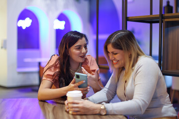 Friends looking mobile phone and smiling at cafe with purple background
