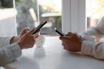 close-up of smart phones in the hands of woman and man sitting on wooden table at coffee shop. Meeting friends. couple using digital gadgets.