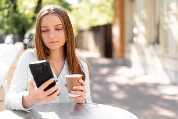 Image of serious young woman chatting on mobile phone while standing at street cafe outdoors