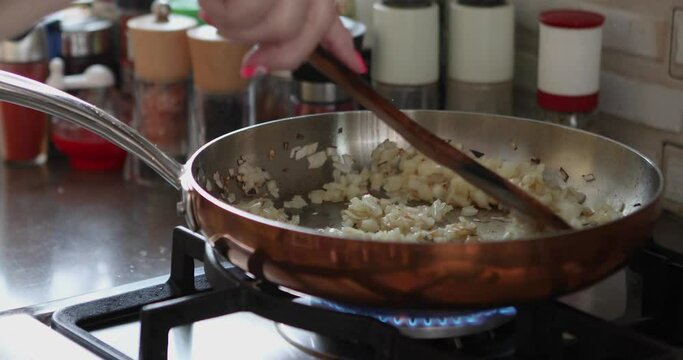 Chef is frying onions in frying pan on gas stove.