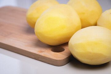 Naklejka na ściany i meble Peeled fresh potatoes lie on a wooden cutting board on a white table