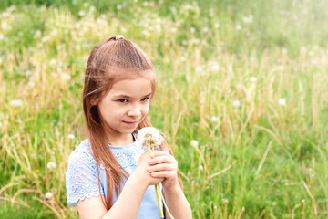 Cute girl with a bouquet of white dandelions and flying seeds against a blurred field of dandelions.