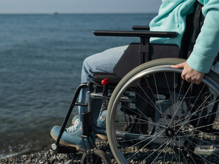 Caucasian woman in a wheelchair on the seashore. Close-up of female hands.