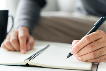left handed man writes in a notebook on the table