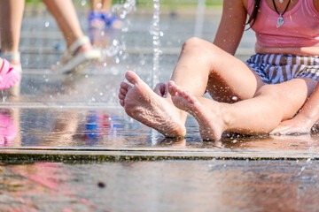 Beautiful feet of a girl sitting in a city fountain. Selective focus. A young woman refreshes herself in jets of cool water on a hot summer day.