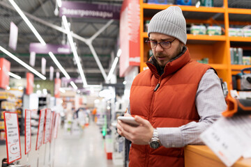 a man in a home goods store examines the assortment on his phone