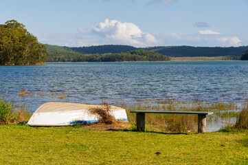 A wooden bench and a rowing boat on the shore of Smiths Lake - Tarbuck Bay, NSW, Australia