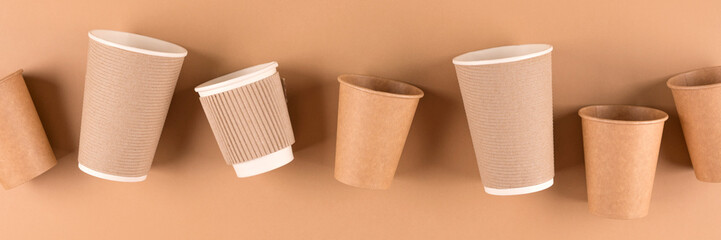 Banner with variety of paper coffee cups over light brown background. Eco paper cups for hot beverages to go. Sustainable take away food packaging concept. Top view