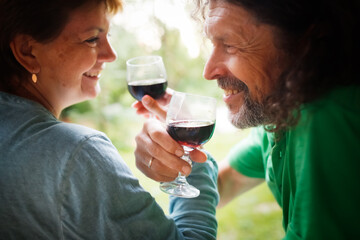 middle-aged couple drinking red wine from glasses outside , hipster man with long hair and beard