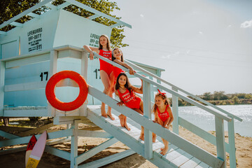 Young girls in red summer bikini posing on blue lifeguard station at the beach