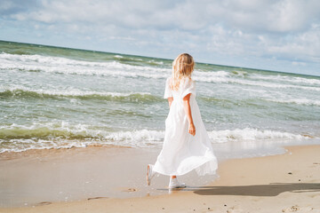 Fototapeta na wymiar Young beautiful woman with long hair in white dress enjoying life on the sea beach